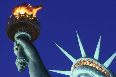 Close-up view focusing on the raised torch and head of the Statue of Liberty against a twilight sky.