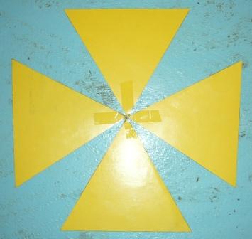 A geometric pattern featuring four yellow triangles pointing towards a central square on a textured blue background, resembling a simplified artistic representation of celestial bodies.