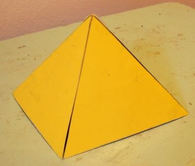 A geometric model of a yellow pyramid with a triangular base, resting on a beige surface.