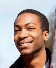 Young African American man smiling broadly, with a clear sky in the background.