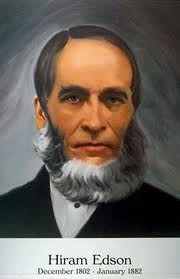 Portrait of an elderly man with a dark suit, white shirt, and black tie. He has a neatly trimmed white beard and serious expression, set against a soft, gray background. Underneath, text reads "Hiram Edson December 1802 - January 1882."