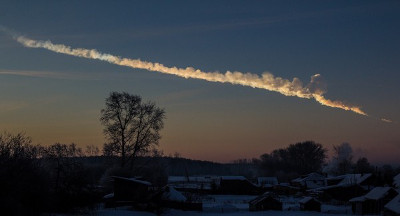 A winter dawn scene over a rural village, showing a striking celestial trail stretching across a twilight sky.