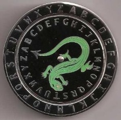 A circular object featuring a stylized green lizard-like creature with a sweeping tail, set against a black background encircled by the letters of the Latin alphabet in silver.