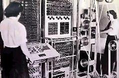 Two women in a mid-20th-century computer room operating and analyzing data on large, early computational machines filled with dials and switches.