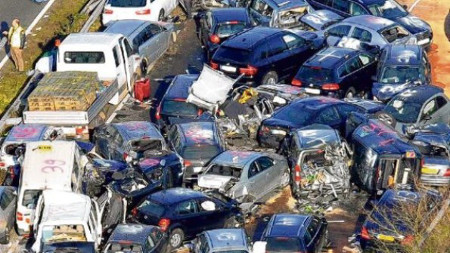 A large vehicular accident on a highway featuring multiple cars and a van crumpled and piled together in disarray, suggesting a severe traffic incident.