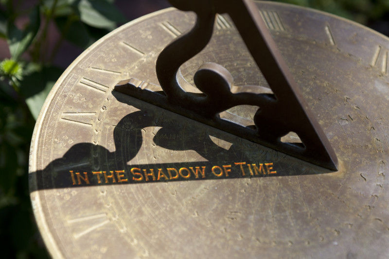 Close-up of a sundial made of brass with a gnomon casting a shadow over engraved letters, which read "IN THE SHADOW OF TIME," surrounded by symbols reminiscent of The Mazzaroth.
