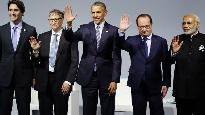 Five male political leaders standing side by side on a stage, each waving to the audience with their right hand raised. They are dressed in formal suits. The central figure is distinguished by his charismatic smile.