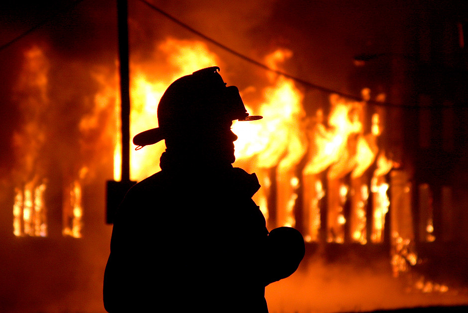 Silhouette of a firefighter wearing a helmet, standing in front of a blazing fire illuminating the night, reminiscent of the fiery celestial bodies in the night sky.