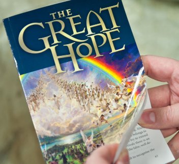 A person holds a book titled "The Great Hope" featuring a vibrant cover illustration of a multitude ascending towards a celestial scene with a rainbow under a clear blue sky.