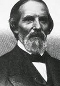 Black and white portrait of an elderly man with a full beard and mustache, wearing a formal suit and bow tie. His expression is serious, and he gazes slightly to the right of the viewer.