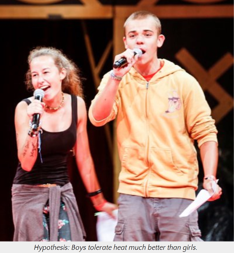 A young man and woman enthusiastically singing into microphones on stage, the woman smiles widely while the man looks intently at the audience. Both are dressed in casual summer clothing.