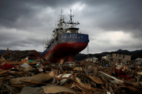 A large blue and red ship stranded on a heap of wooden debris under a cloudy sky, suggesting a catastrophic event.