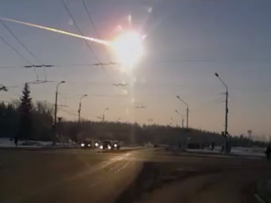 A celestial event captured over a busy roadway, featuring a bright, fiery trail in the sky, possibly a meteor, alongside the sun casting rays over the landscape dotted with street lights and driving cars.