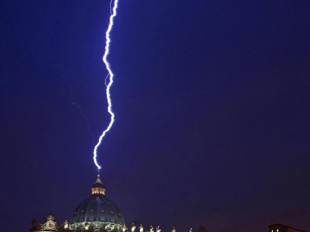 A vivid lightning bolt striking the dome of a large building against a dark, twilight sky.