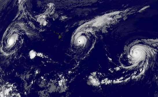 Satellite image showing multiple hurricane formations over an ocean, demonstrating the powerful swirling patterns of clouds as viewed from space.