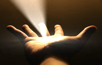 An open human hand facing upwards, illuminated by a dramatic beam of light that appears to emanate directly from the palm, set against a dark background.