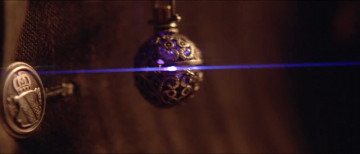 An ornate spherical pendant, reminiscent of celestial globes used in studying the heavens, hangs on a delicate chain against a dark, textured background. A horizontal blue light beam intersects the scene, suggesting a mystical or scientific observation theme.