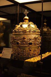 An intricately designed golden artifact, resembling an ornate celestial globe, displayed under a spotlight in a museum setting, featuring symbolic decorations inspired by the Mazzaroth.
