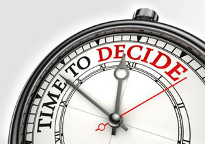 Close-up of a vintage-style stopwatch with the text "TIME TO DECIDE" highlighted in red on the clock face, pointing at 12 o'clock. The hands of the clock align closely, indicating a significant moment.