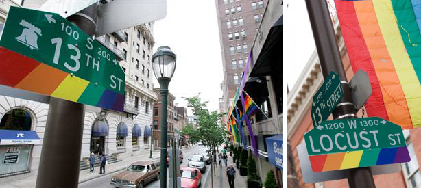 A cityscape view featuring two street signs, "13th St" and "Locust St", adorned with rainbow colors, against an urban street background with cars and trees.