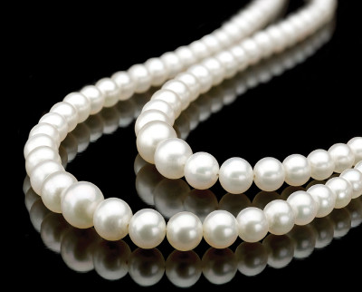 A string of white pearls elegantly displayed on a reflective black surface, showing smooth, round beads with a lustrous finish.