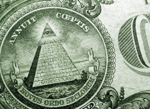 Close-up view of a detailed illustration featuring a pyramid with an eye enclosed in a triangle at the top, seen on the back of a U.S. dollar bill. The pyramid is surrounded by Latin phrases and intricate designs.