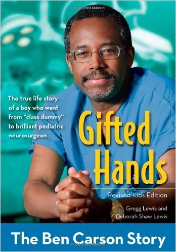 Cover of the book "Gifted Hands: The Ben Carson Story," featuring an image of Dr. Ben Carson in a blue surgical scrub top, wearing glasses, with his arms crossed, backed by a pale blue background with a blurred medical environment.