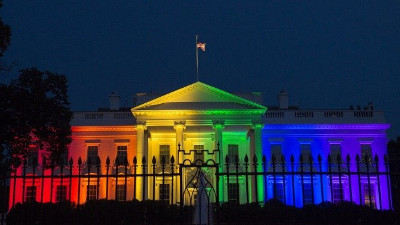The White House illuminated with a spectrum of light colors from violet to red, resembling the dispersion of light, under a night sky.