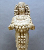 Ivory figurine of a woman adorned with intricate carvings and multiple rows of beads, standing with outstretched arms.