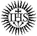 A black and white symbol featuring a stylized sun with rays and a central motif of the monogram "IHS" above a cross, embedded within a three-lined emblem resembling a stylized interpretation of the Mazzaroth.