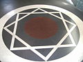 A geometric pattern featuring a large circle containing overlapping triangles that form a six-pointed star, set against a black background encircled by a white band.